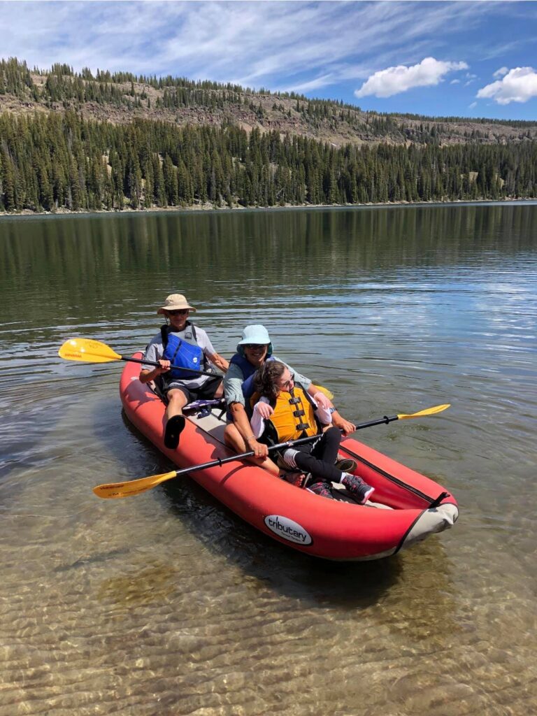 Three people sit in an inflatable raft preparing to paddle during an adaptive water recreation program