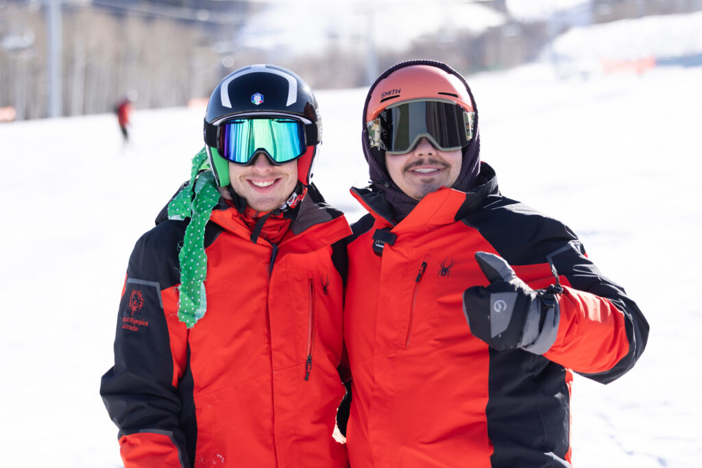 Two Team Powderhorn participants stand together on a snowy slope, smiling and posing for a photo.