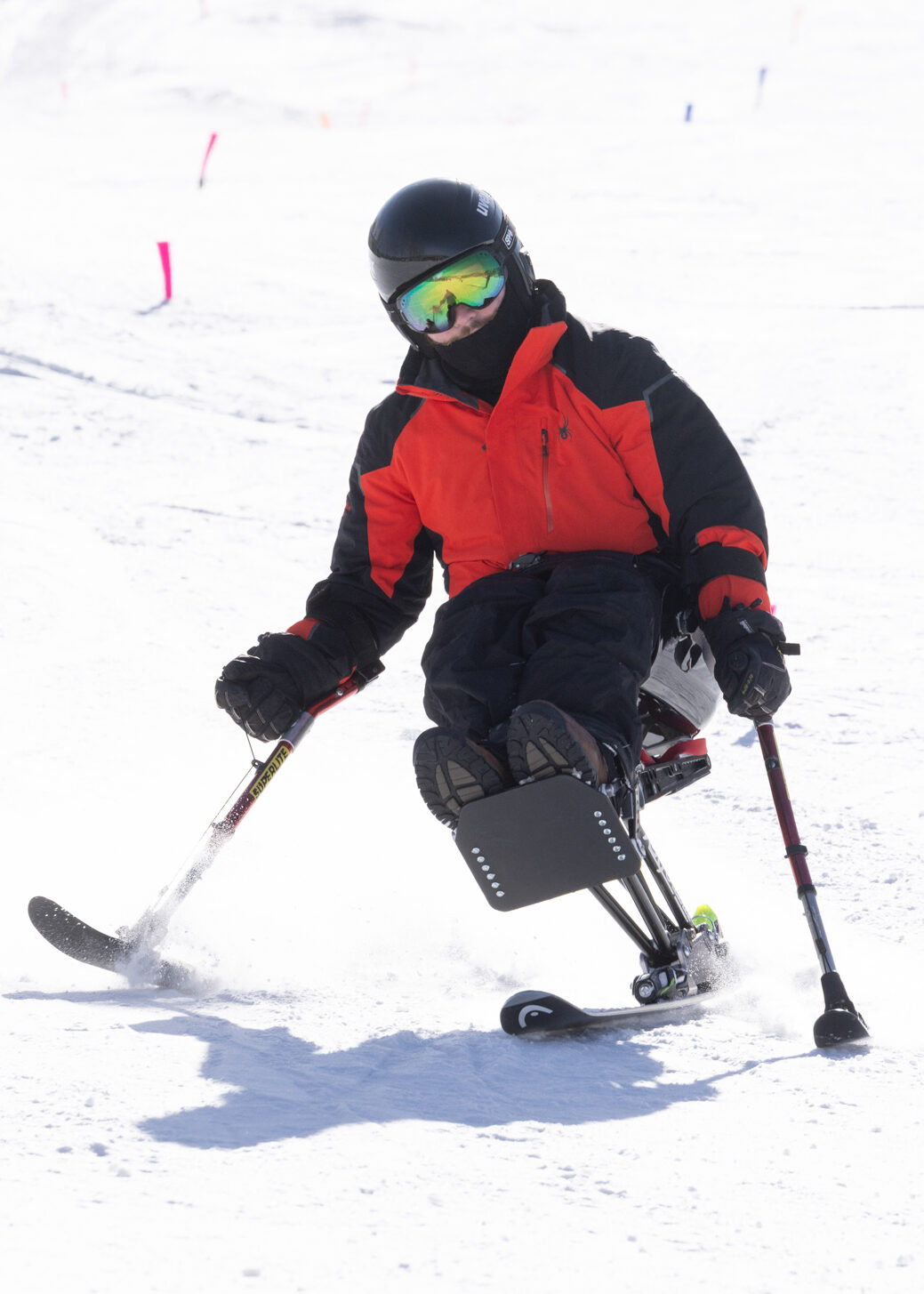 A skier uses a sit-ski and outriggers to turn on a snowy slope during an adaptive skiing program