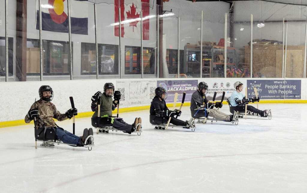Sled Hockey participants line up in a row on the ice awaiting instruction
