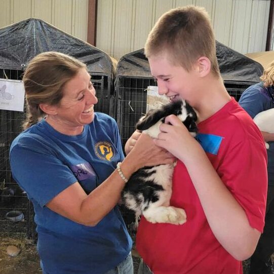 Participant holding a rabbit with guidance from Harmony Acres staff
